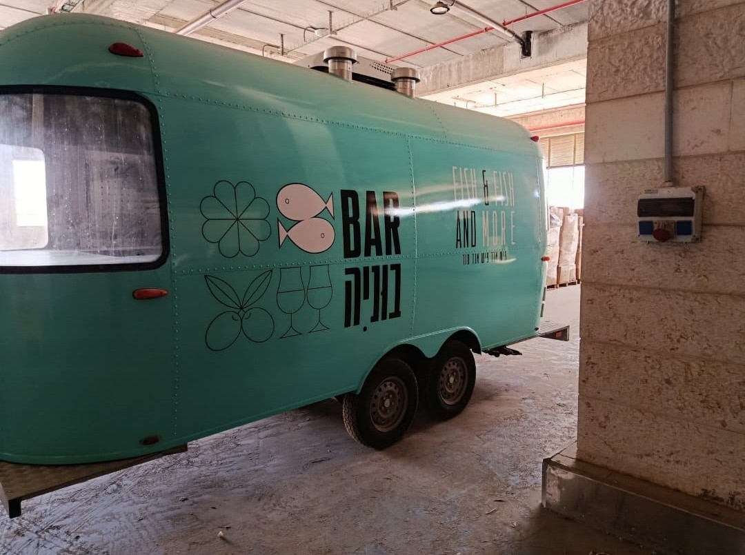 A rear three-quarter view of the turquoise street food trailer in the workshop.